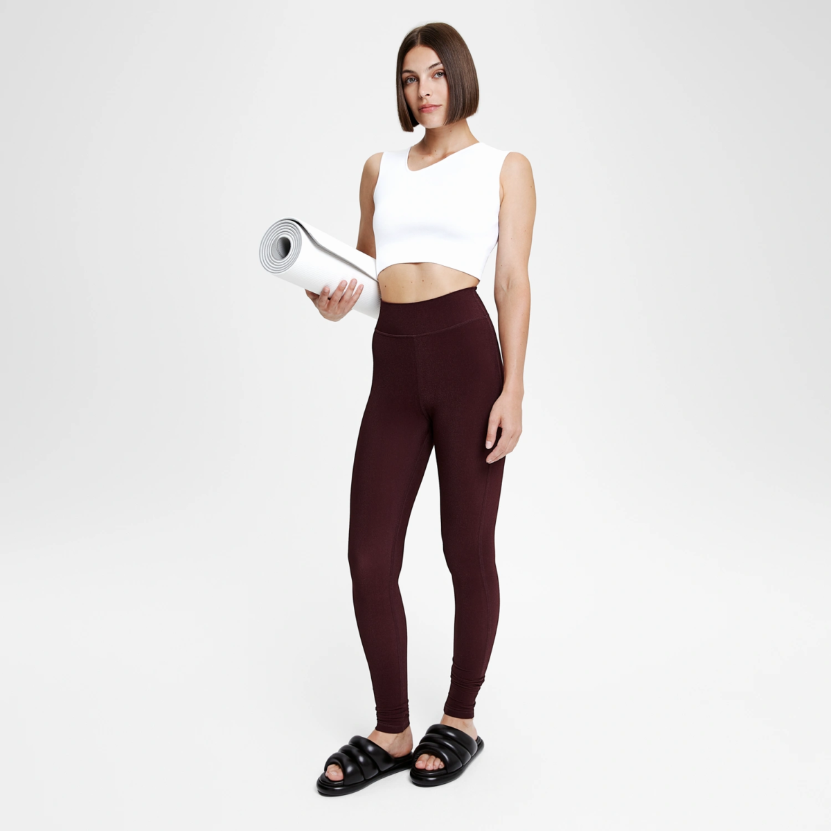 Femme tenant un tapis de yoga en legging rouge bordeaux coupe sportive, tenue sport chic