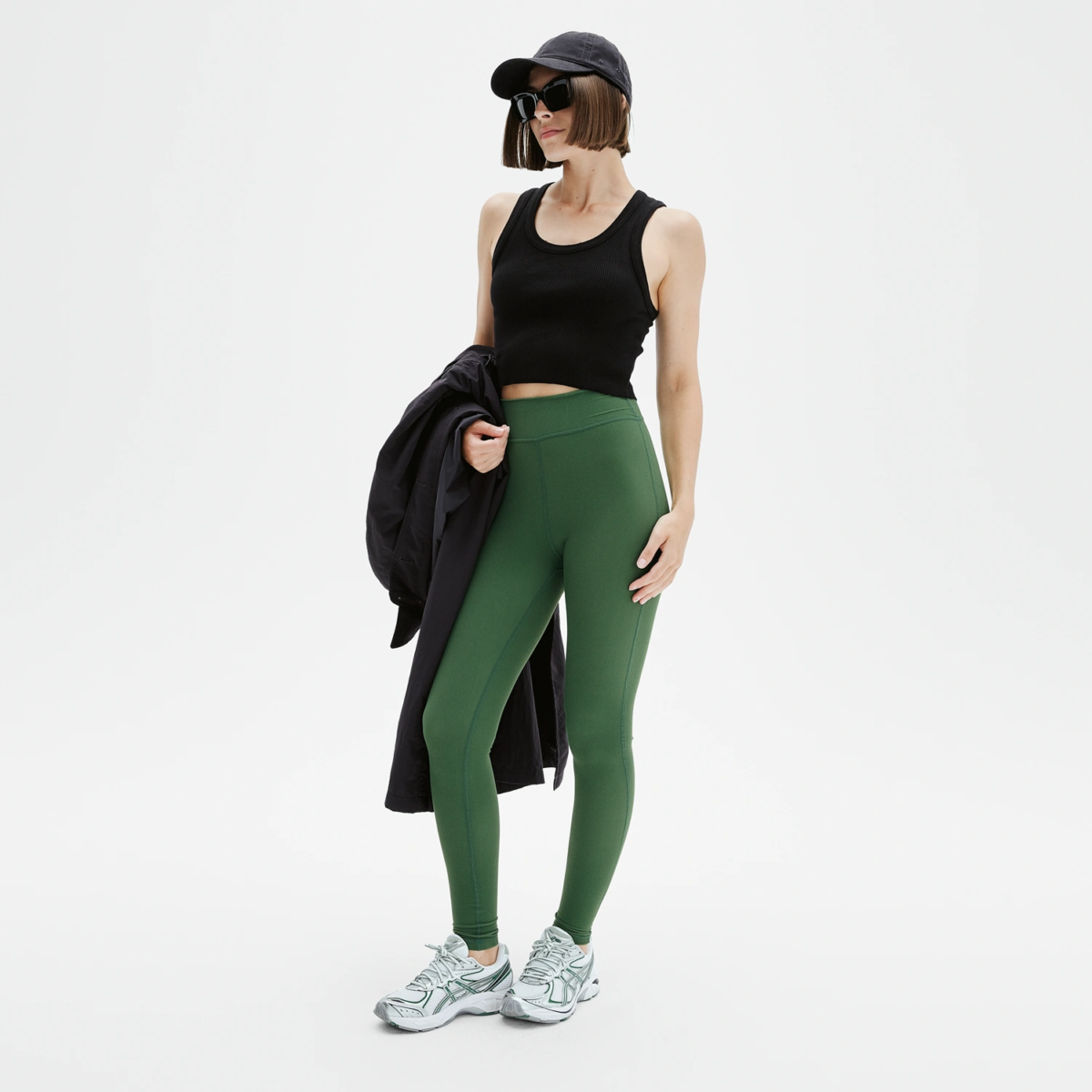 Femme portant legging yoga vert forest green coupe sportive, look casual chic avec trench noir et sneakers, Pattes de Velours Paris