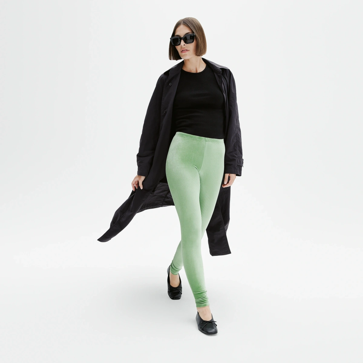 Legging vert amande en velours côtelé, silhouette féminine en mouvement avec manteau fluide noir